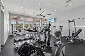 A spacious gym with treadmills, elliptical machines, and a ceiling fan.