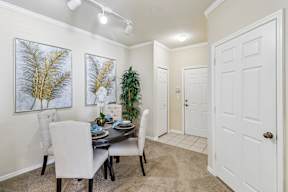 A dining room with a table set for two and a potted plant.
