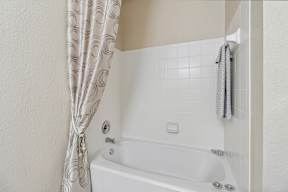 A white bathtub with a shower curtain and a towel hanging on the wall.