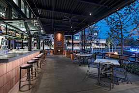 A restaurant with tables and chairs under a roof with a glass wall.
