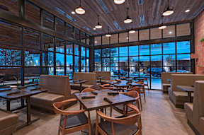 A restaurant with wooden tables and chairs and a view of the street outside.