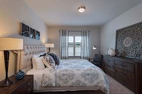 A bedroom with a large bed, a lamp, and a window with curtains.