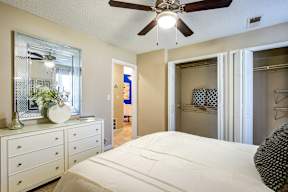 A bedroom with a large bed, a dresser with a mirror, and a ceiling fan.