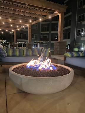 A fire pit with flames burning in the middle of a patio.