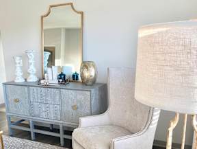 A grey dresser with a mirror above it and a chair with a lamp beside it.