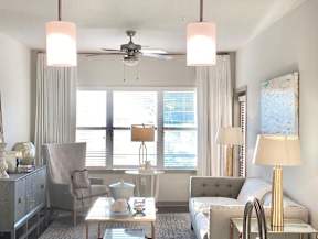 A living room with a grey couch, a white armchair, a glass coffee table, and a ceiling fan.