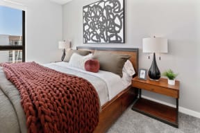 a bedroom with a bed and a table with lamps and a window