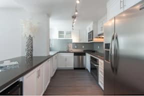A modern kitchen with a stainless steel refrigerator and wooden flooring.
