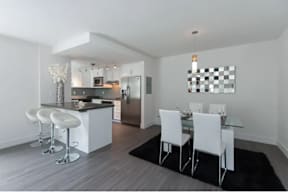 A modern kitchen with white chairs and a glass table.