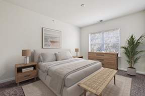 A bedroom with a bed, nightstand, and a plant.