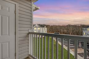 A white door is open to a balcony with a view of a house and trees.