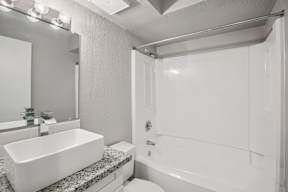 A white bathroom with a sink, mirror, and bathtub.