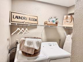 A laundry room with a washer and dryer, a basket with towels, and a sign on the wall.