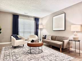 A living room with a white chair, a brown coffee table, a beige couch, and a grey rug.