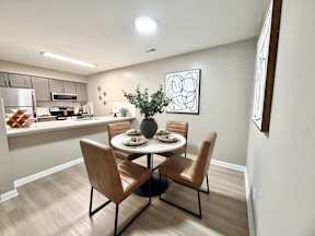 A dining room with a table set for two and a kitchen area in the background.