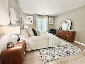 A bedroom with a large bed, a wooden nightstand, and a rug on the floor.