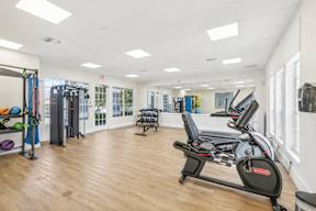 A gym with a row of treadmilers and a squat rack.