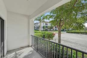 A balcony with a metal railing overlooks a tree and a street.