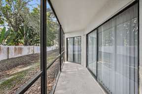 A long, narrow balcony with glass railings and a view of trees and a fence.