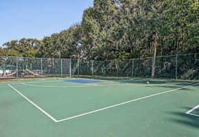A tennis court surrounded by a fence and trees.