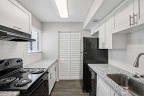 A black refrigerator stands in a kitchen with white cabinets and a black stove.