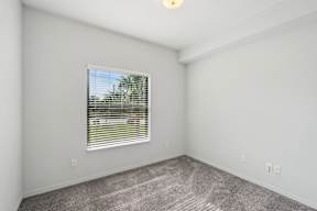 A room with a window covered by blinds and a grey carpet.
