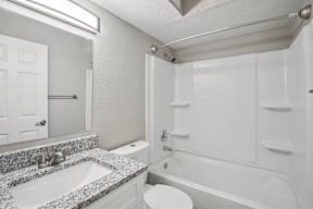 A white bathroom with a granite countertop and a white bathtub.
