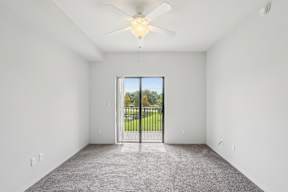 A room with a ceiling fan and a sliding glass door leading to a backyard.