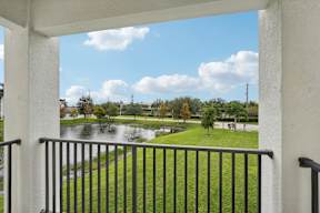 A balcony overlooks a green lawn and a body of water.