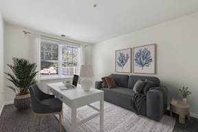 A modern living room with a grey sofa, a white desk, and a potted plant.