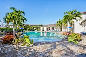 A pool surrounded by palm trees and green chairs.