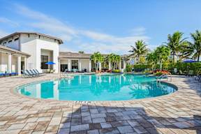 A swimming pool surrounded by a tiled patio and a white building with a balcony.