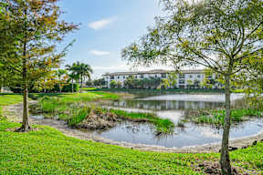 A serene park with a pond, trees, and a building in the background.
