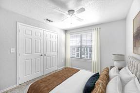 A bedroom with a bed, a ceiling fan, and a window with curtains.