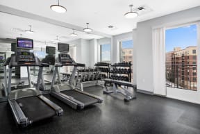 a gym with cardio equipment and a window with a view of the city