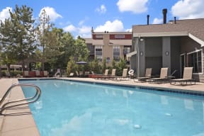 a swimming pool with chairs and a building in the background