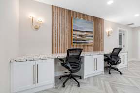 Two black chairs are placed in front of a desk with a painting on the wall.