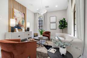 A living room with a brown chair, a white chair, a black coffee table, and a large painting on the wall.
