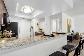 A modern kitchen with a marble countertop and black chairs.