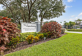 A sign that says The Sanctuary at Highland Oaks is surrounded by green grass and shrubbery.