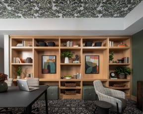 a room with a desk with a laptop and a bookshelf