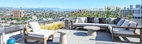 A patio with a couch, chairs, and a table overlooking a city.