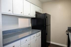 A black refrigerator is in a kitchen with white cabinets.