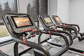 A row of treadmills with screens on the back of the seat.