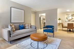 A living room with a beige couch, a blue chair, and a brown ottoman.