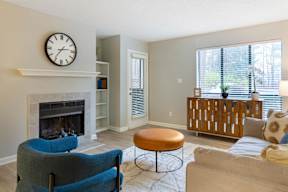 A living room with a fireplace, a blue chair, a brown ottoman, and a white couch.