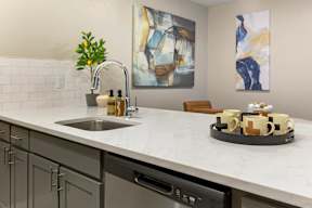 A kitchen with a sink, a tray of mugs, and two paintings on the wall.