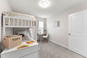 A white bunk bed with a basket labeled "TOYS" on top of a white dresser in a room with a desk and chair.