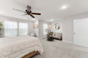 A bedroom with a bed, a couch, a ceiling fan, and a mirror.