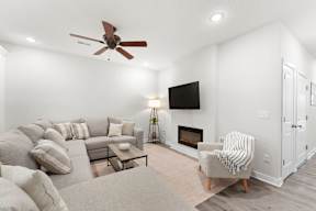 A living room with a grey couch, a coffee table, a fireplace, and a ceiling fan.